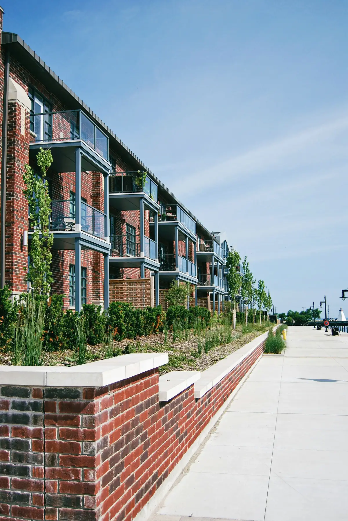 A brick residential building with balconies along a planted walkway