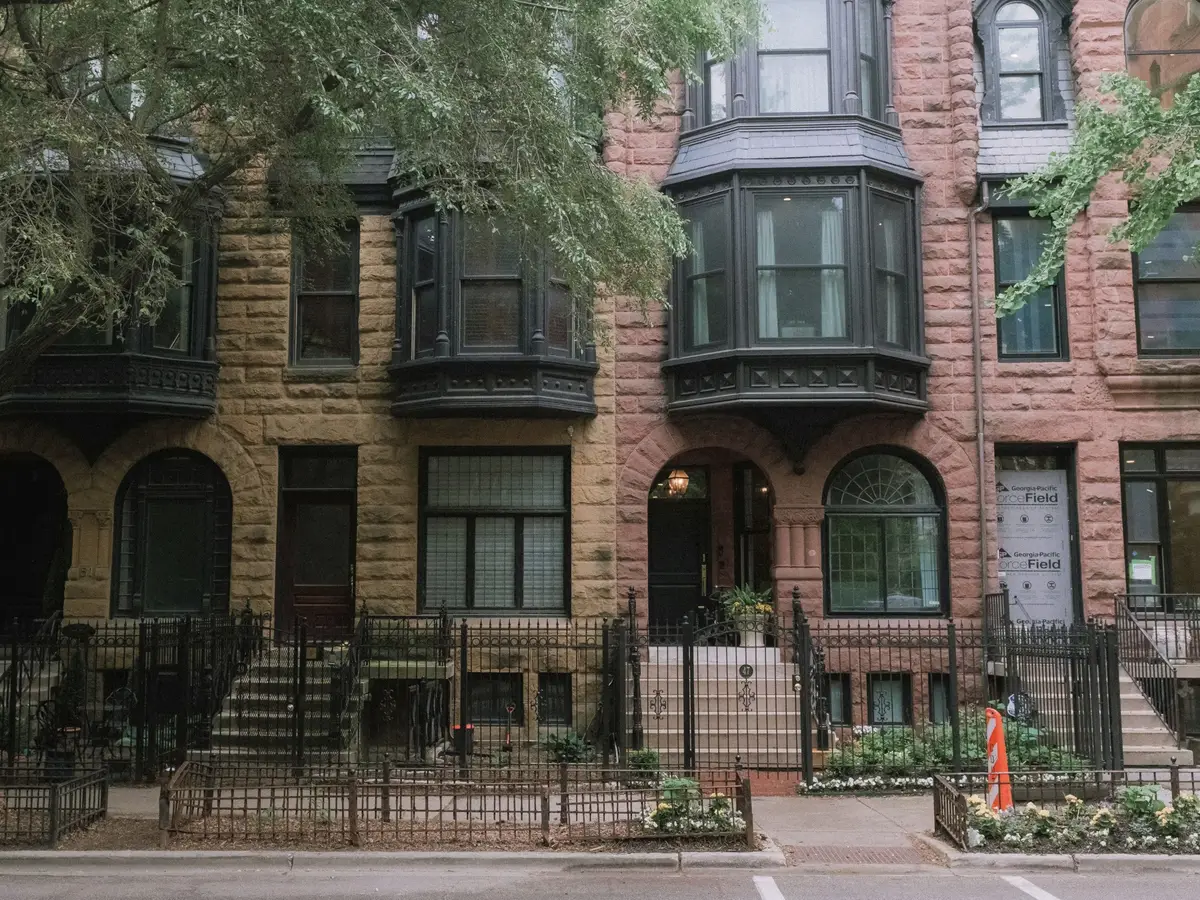 Brownstone and brick row houses with bay windows behind trees