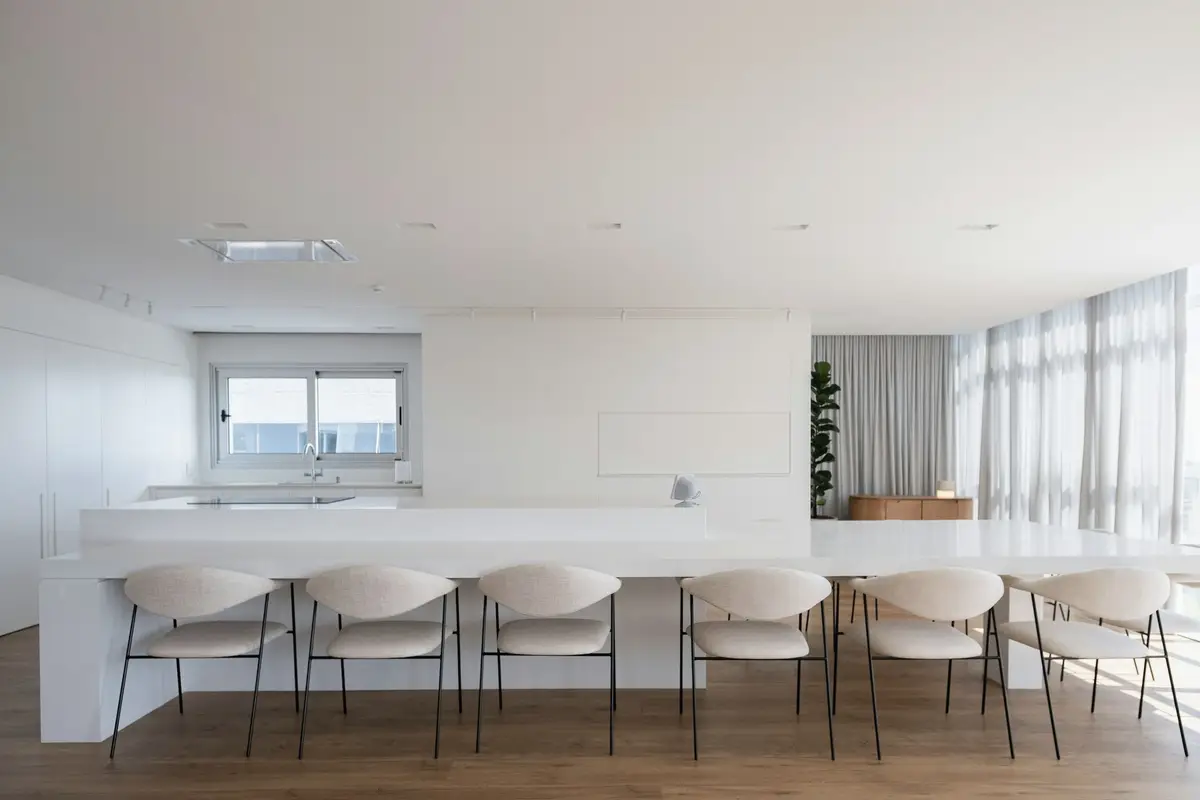 A bright kitchen with a long white island and chairs